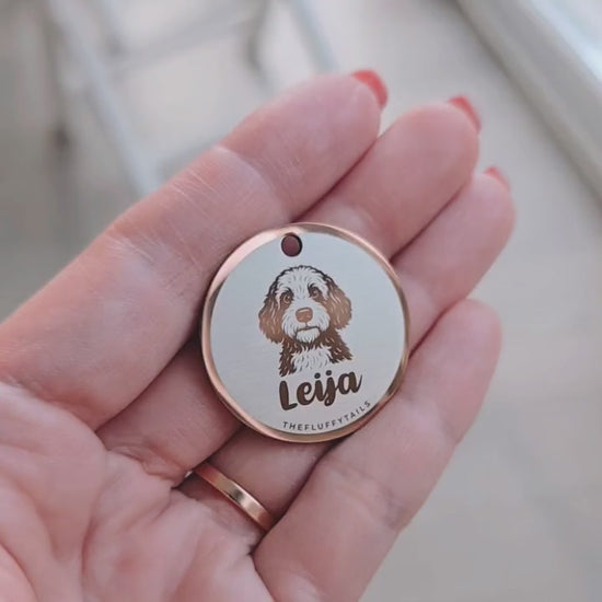 Video som visar en rund roséguldfärgad namnbricka med ikon av spansk vattenhund och hundens namn i skrivstål. Namnbrickan vinklas i ljuset för att visa dess spegelblanka yta och reflektioner.