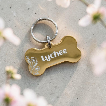 Guldfärgad hundbricka i hundbensform av rostfritt stål med blommigt motiv och hundens namn graverat 