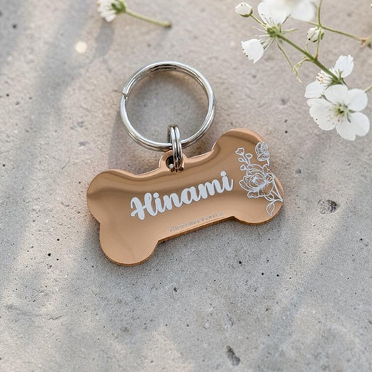 Roséguldfärgad hundbensformad hundbricka med blommigt motiv av pioner och hundens namn graverat 