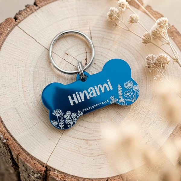 Blå hundbricka i hundbensform med vita blommor och hundens namn graverat 